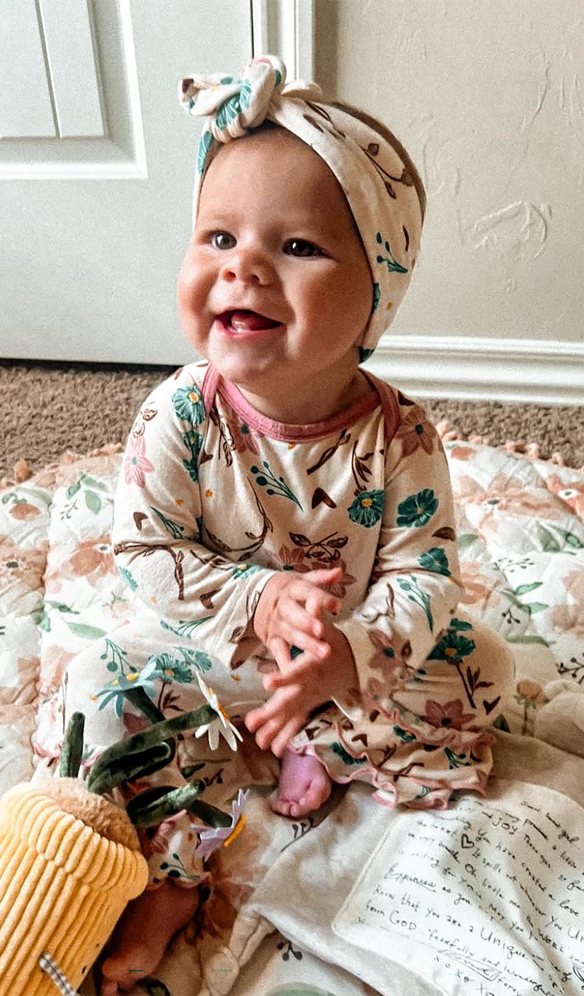 Magnolia Ruffle Romper and matching headwrap worn by smiling baby girl sitting on a blanket.