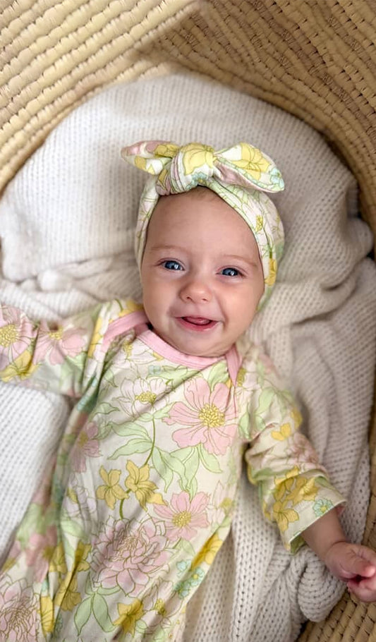 Baby in a Begonia floral outfit and headband lying on a soft blanket.