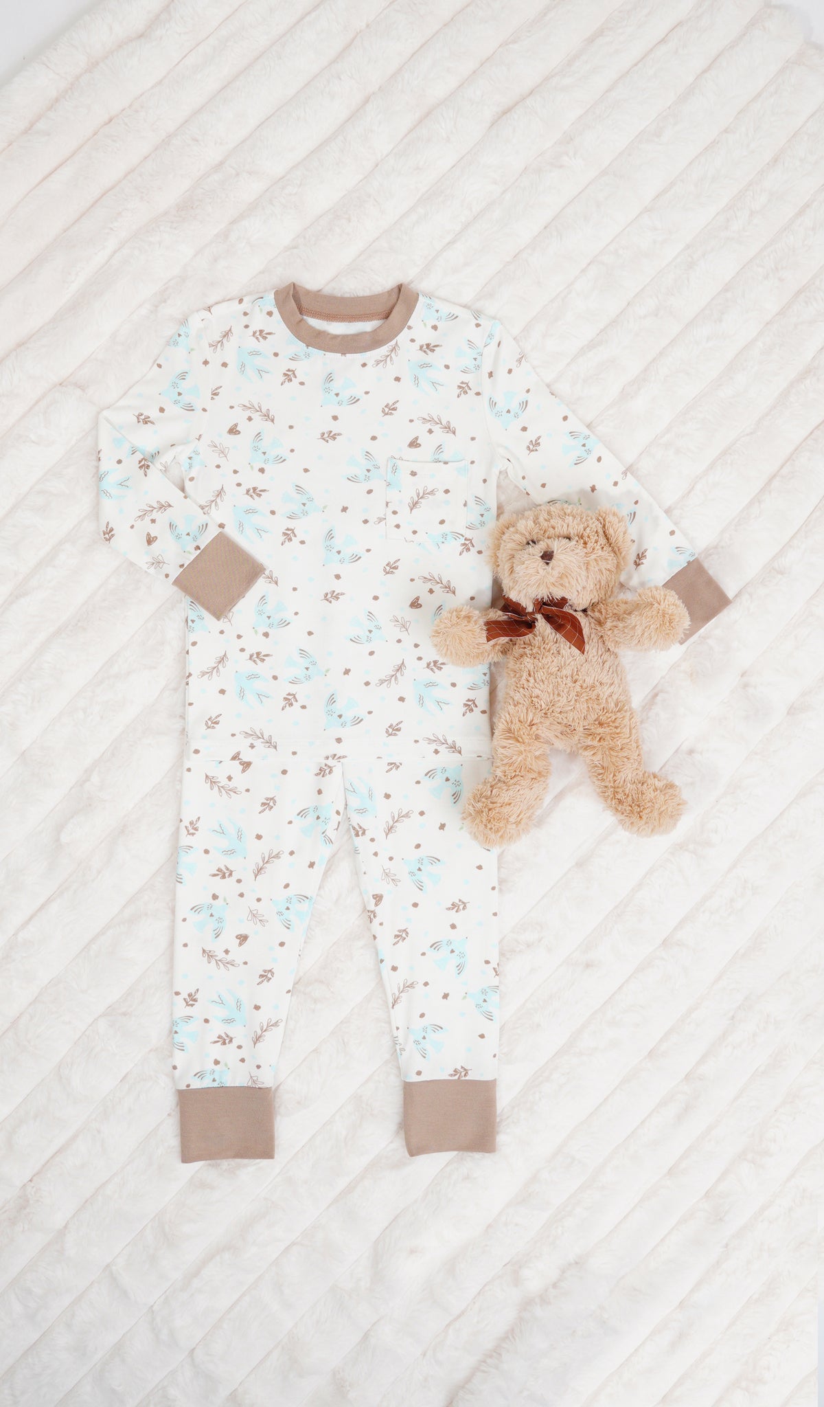 Nest Emerson Kids 2-Piece Pant PJ. Long sleeve top with cuff trim and long pant with cuff trim and a stuffed bear on a soft beige blanket.