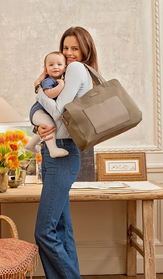 Storksak Juliette Diaper Bag Moss carried by woman holding her baby.