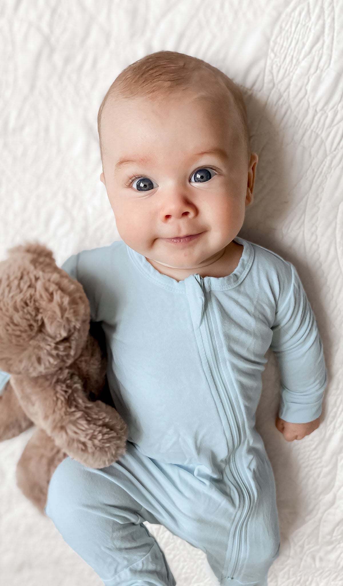 Whispering Blue Footie 2-Piece worn by baby holding teddy bear while laying on a quilt.