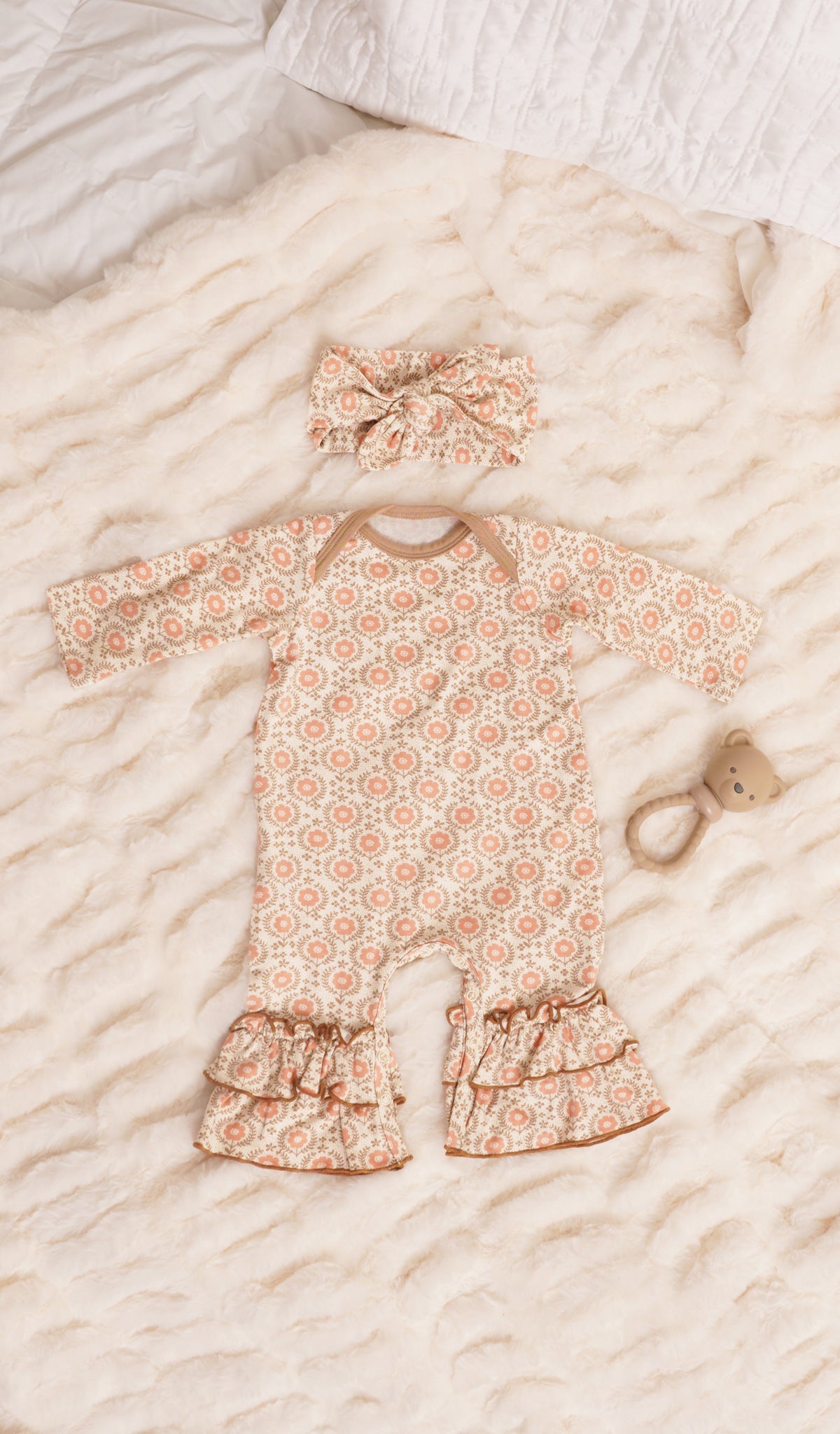 Bohemian Ruffle Romper 2-Piece. Long sleeve romper with ruffles on legs with matching headwrap and a rattle on soft beige bedding.