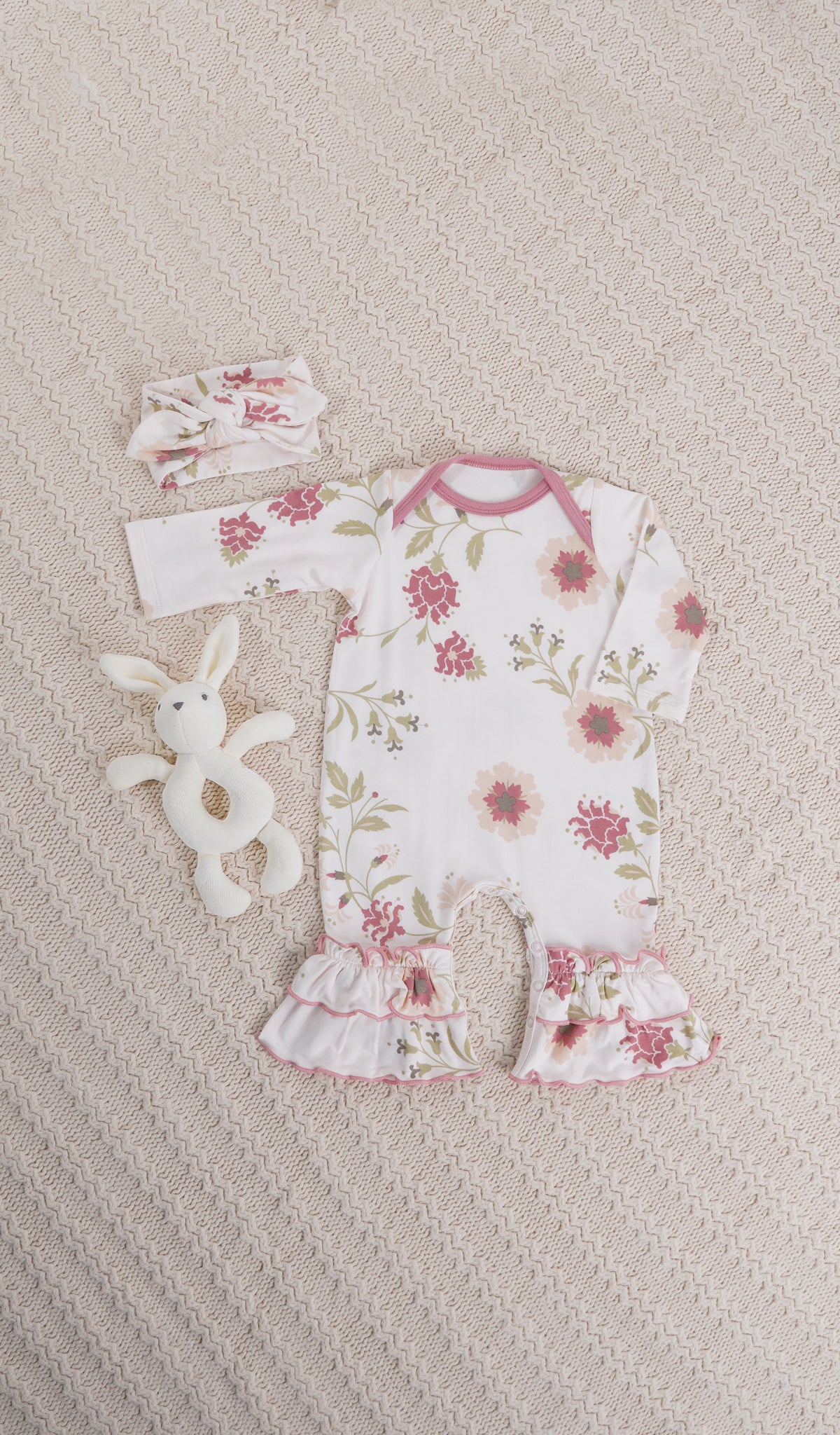Cottage Floral Ruffle Romper 2-Piece. Long sleeve romper with ruffles on legs with matching headwrap and a bunny rattle on knitted beige blanket.