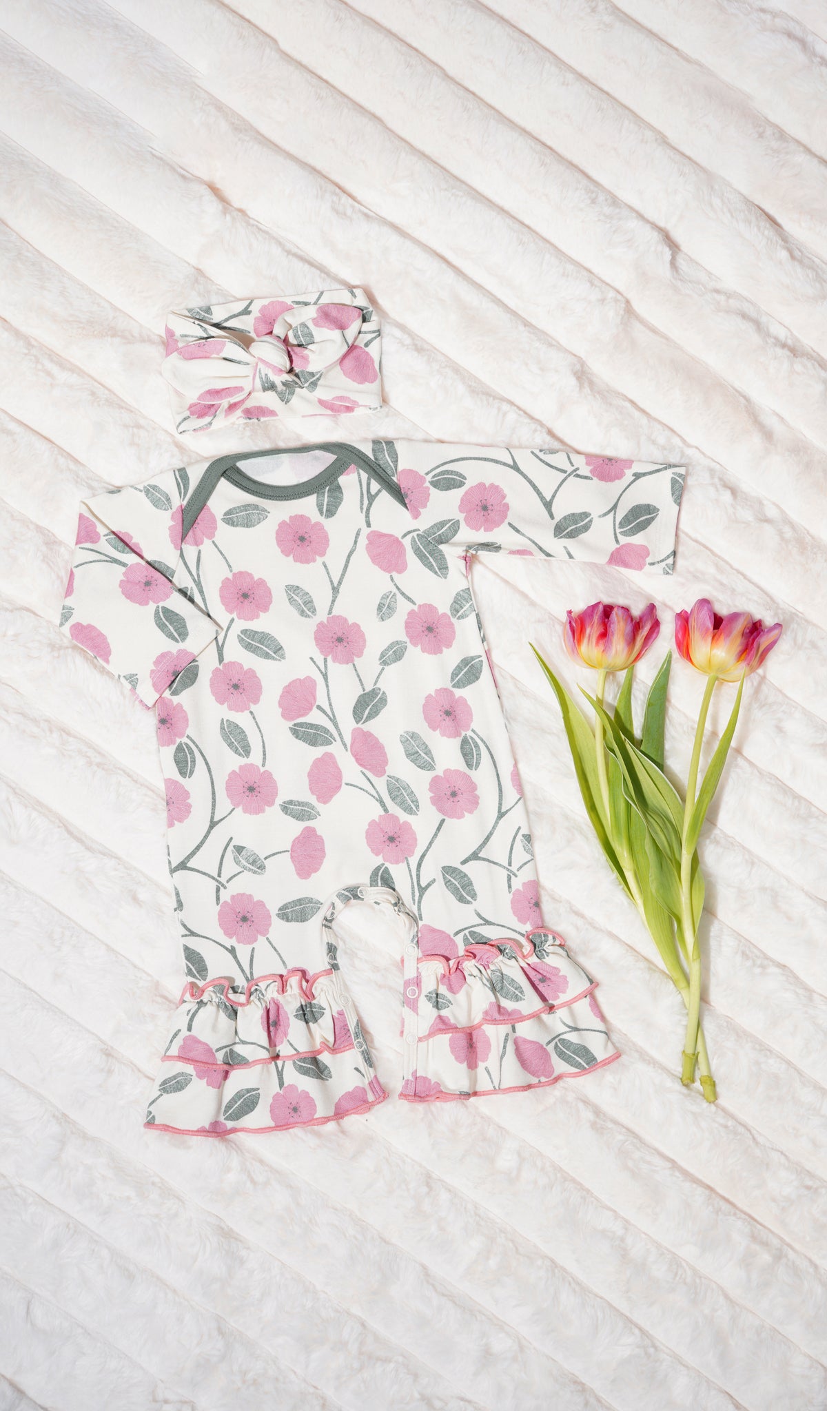 Honey Bloom Ruffle Romper 2-Piece. Long sleeve romper with ruffles on legs with matching headwrap and flowers on soft beige blanket.