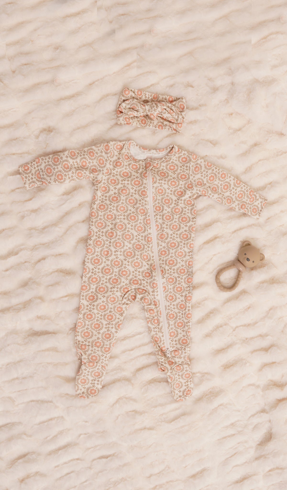 Bohemian Footie 2-Piece Set. Zip front footie for baby with matching headwrap and a rattle on soft beige bedding.