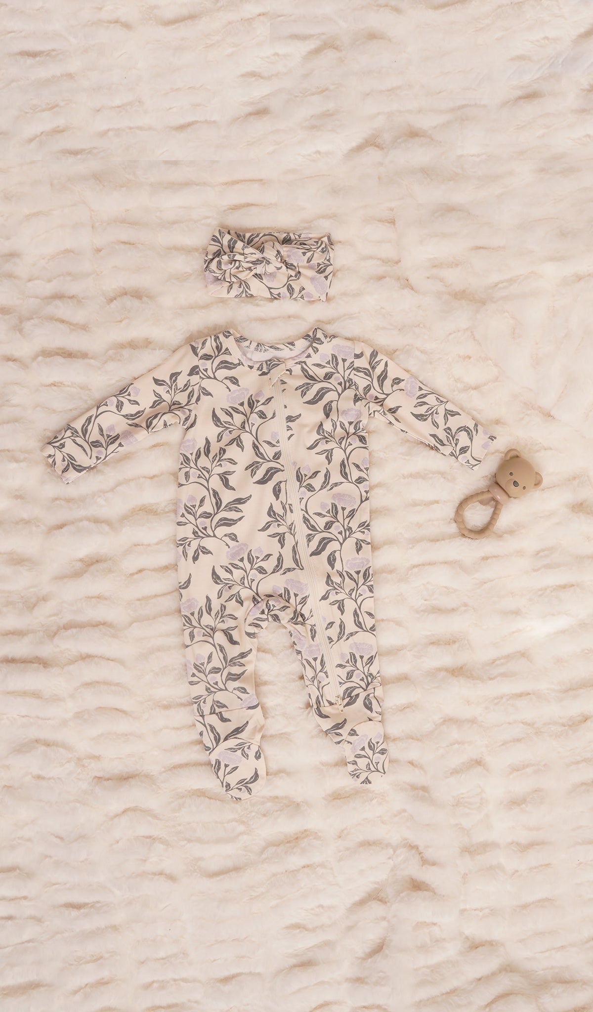 Poppy Footie 2-Piece Set. Zip front footie for baby with matching headwrap and a rattle on soft beige bedding.