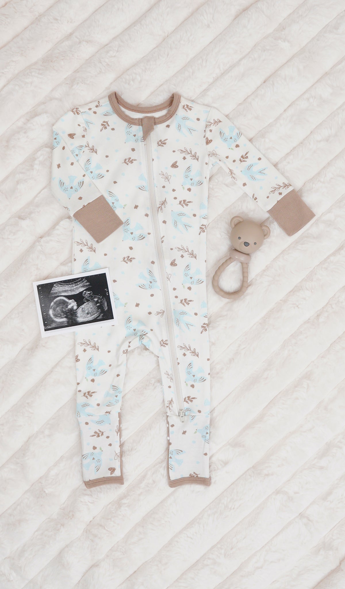 Nest Convertible Romper with long sleeves and zip front on soft beige blanket with rattle and ultra sound image.