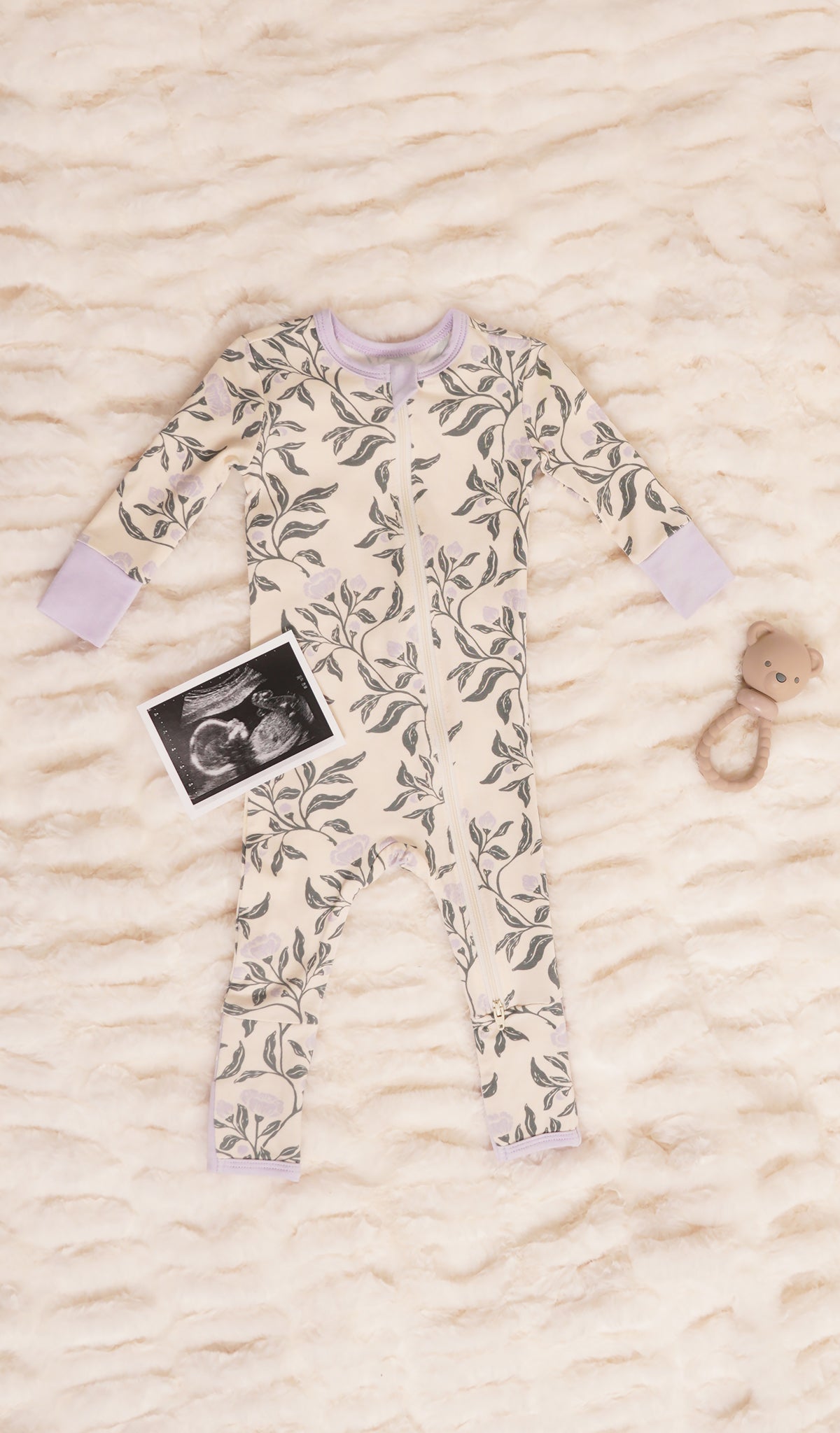 Poppy Convertible Romper with long sleeves and zip front on soft beige bedding with rattle and ultra sound image.