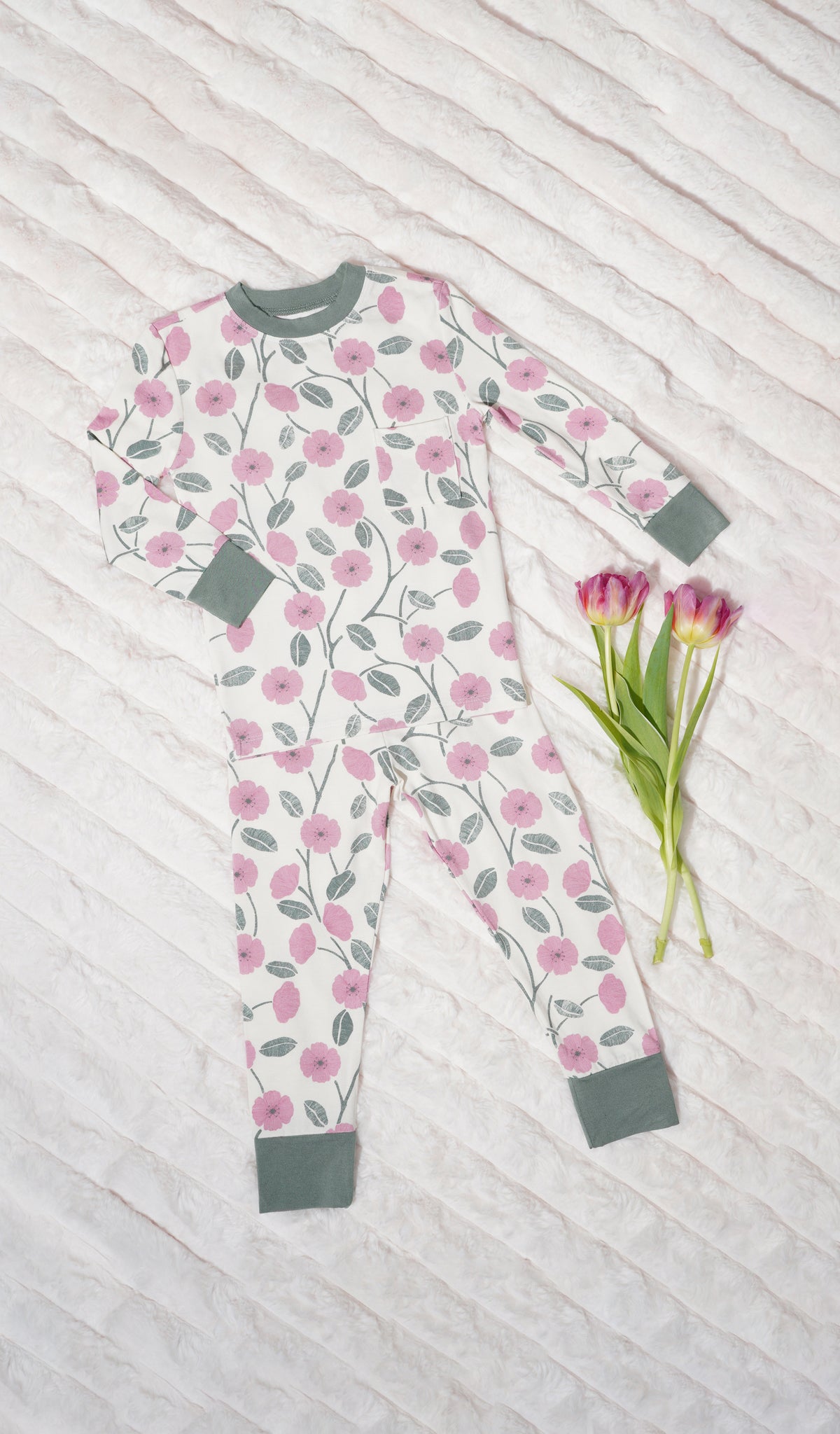Honey Bloom Emerson Kids 2-Piece Pant PJ. Long sleeve top with cuff trim and long pant with cuff trim with flowers on a soft beige blanket.