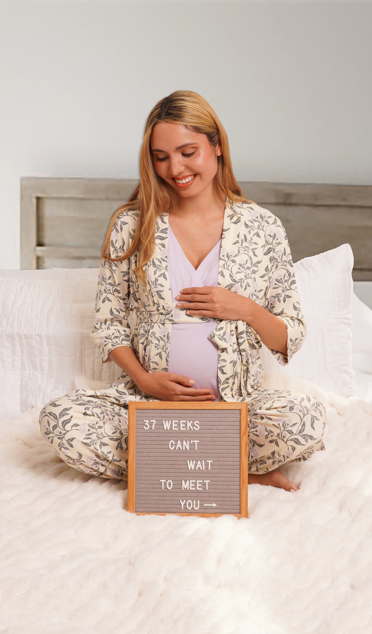 Poppy Analise 5-Piece Set, woman wearing robe, tank top and pant sitting cross legged on a bed holding belly with sign in front of her with pregnancy week count.