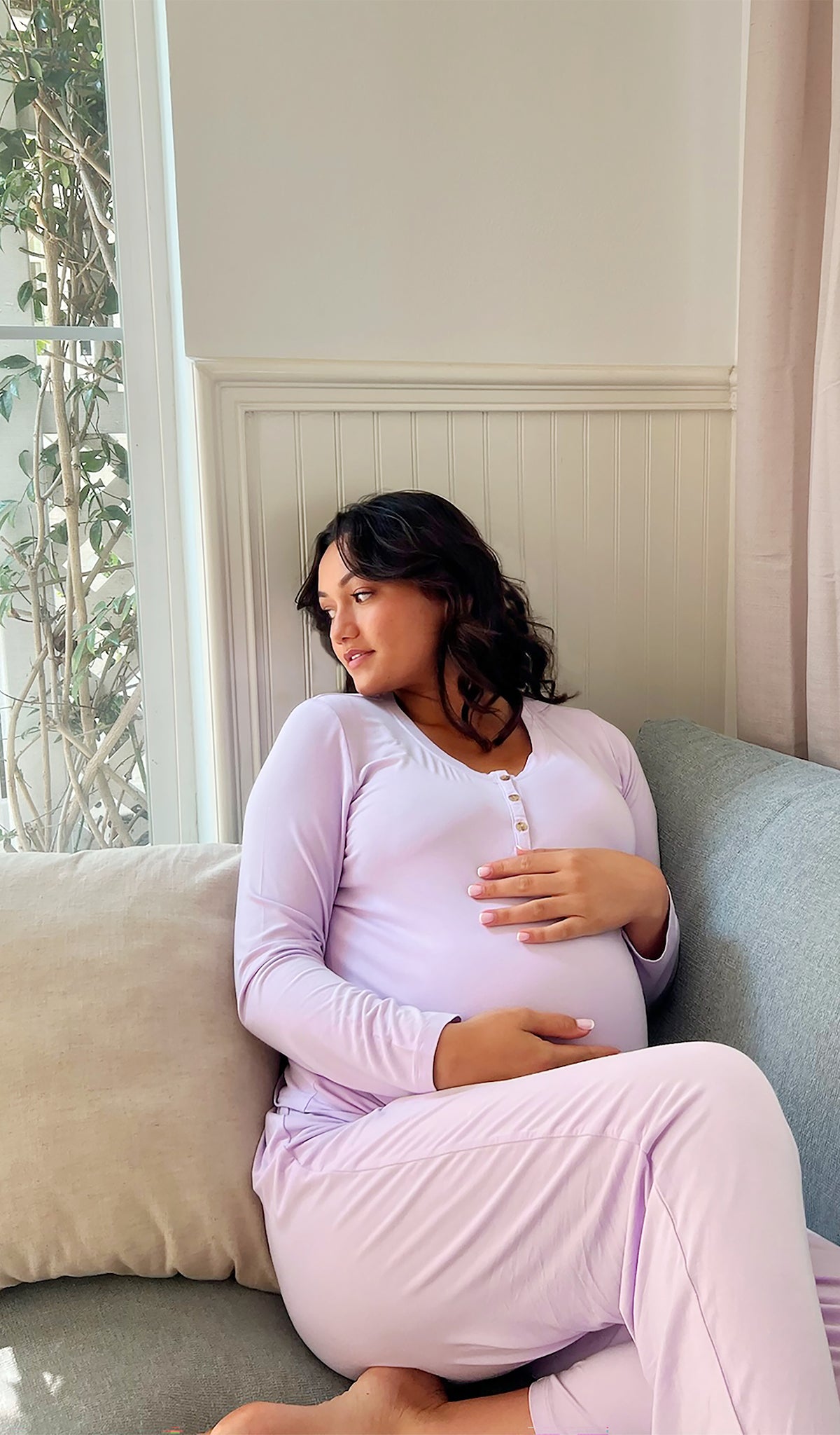 Lavender Laina 2-Piece worn by pregnant woman sitting on sofa looking to the side with both hands on belly.